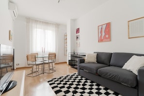 A modern living room with a grey sofa, a glass dining table with chairs, a black and white rug, and a TV. - GuestHost - Bright 66mq apartment equipped with every comfort to comfortably host 4 people. The accommodation is located on the 1th floor with lift (stairs to access it) of a building, in a quiet residential area. The area is equipped with all services a (Milan)