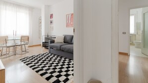 Una sala moderna con un sofá, una mesa de comedor con sillas, un tapete blanco y negro y una puerta de vidrio que da a un baño.