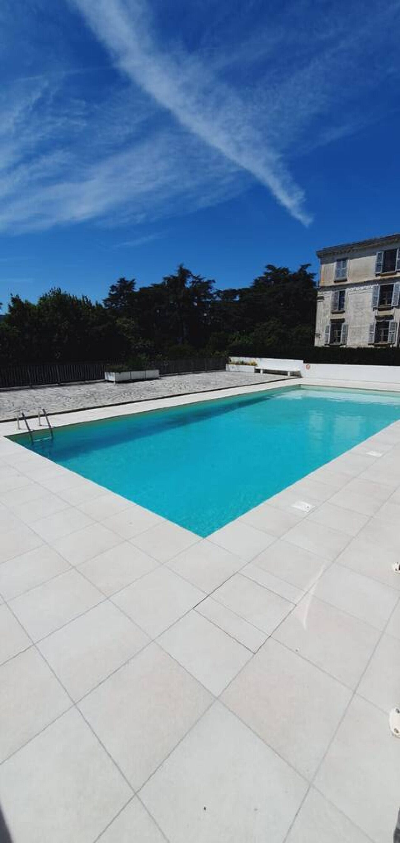 A rectangular swimming pool with clear blue water, surrounded by white tiled flooring.
