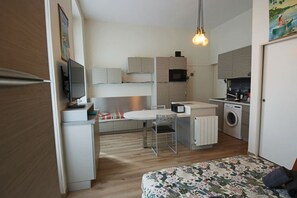 A compact kitchen with a microwave, a washing machine, and a dining area with a table and chairs. - Studio 25m², en hyper centre-ville (Aix-les-Bains)