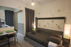 A bedroom with a bed, a desk, a chair, a lamp, and a wall with a floral pattern. - Studio 15m², avec terrasse et place de parking (Aix-les-Bains)