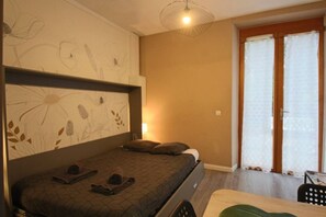 A bedroom with a bed, a headboard with floral artwork, a bedside table, and a window with curtains.