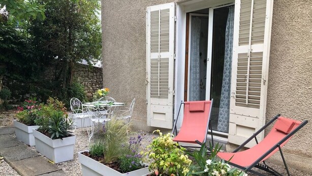 A patio with planters, outdoor furniture, and a building with shutters.