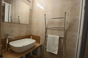 A bathroom with a large sink, a towel rack, and a shower area.
