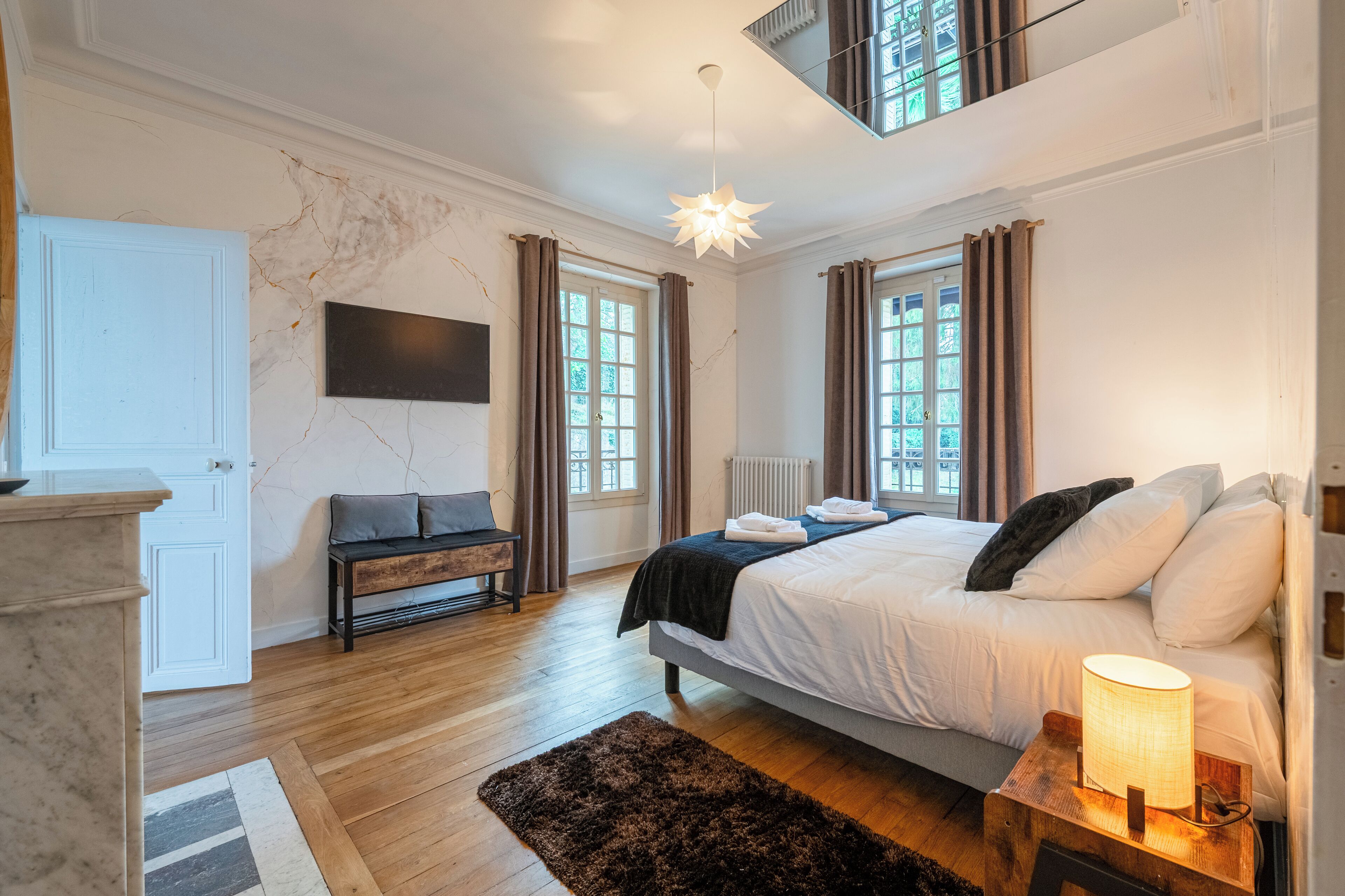 A bedroom with a bed, bedside lamp, and a view of the outdoors through windows.