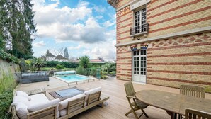 A wooden deck with a pool, outdoor furniture, and a brick building with a window and door.