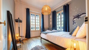 A bedroom with a bed, a hanging light fixture, a radiator, and a window with curtains.