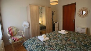 Un dormitorio con cama, una silla, armario, espejo y lámpara colgante.
