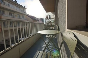 A balcony with a round table and two chairs, overlooking a cityscape with buildings and scaffolding. - Appartement 55m², 1 chambre, centre-ville, garage (Aix-les-Bains)
