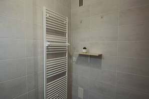 A bathroom with a white towel rack, a small shelf with a potted plant, and tiled walls. - Appartement 55m², 1 chambre, centre-ville, garage (Aix-les-Bains)