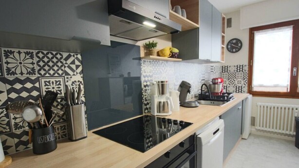 Una cocina moderna con estufa negra, utensilios de acero inoxidable, cafetera y baldosas estampadas.