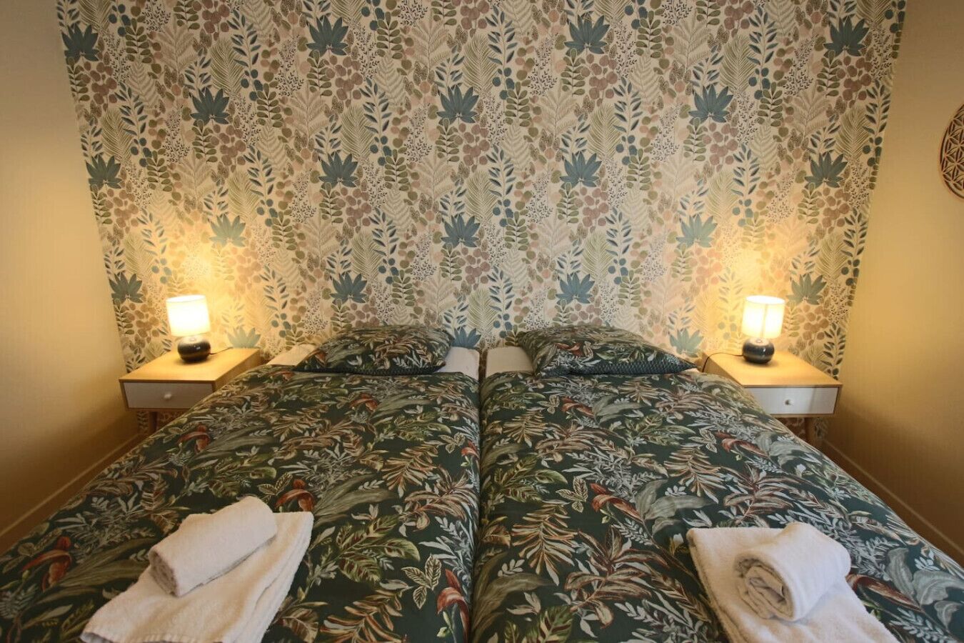 Een tweepersoonsbed met bloemenbeddengoed, twee bedlampjes en een decoratief wandtapijt.