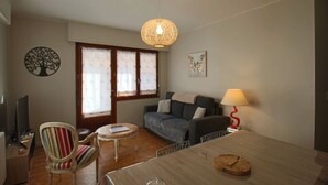 Una sala de estar con sofá, mesa de comedor, silla, lámpara y televisor.