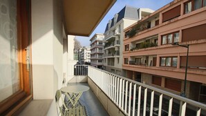 Un balcón con una mesa y sillas, vistas a edificios vecinos y una barandilla de metal.