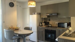 Uma cozinha compacta com área de refeições, incluindo geladeira, micro-ondas, fogão e luminária pendente.