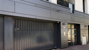 Um edifício moderno com uma grande porta de garagem metálica, entrada de vidro e uma varanda florida.