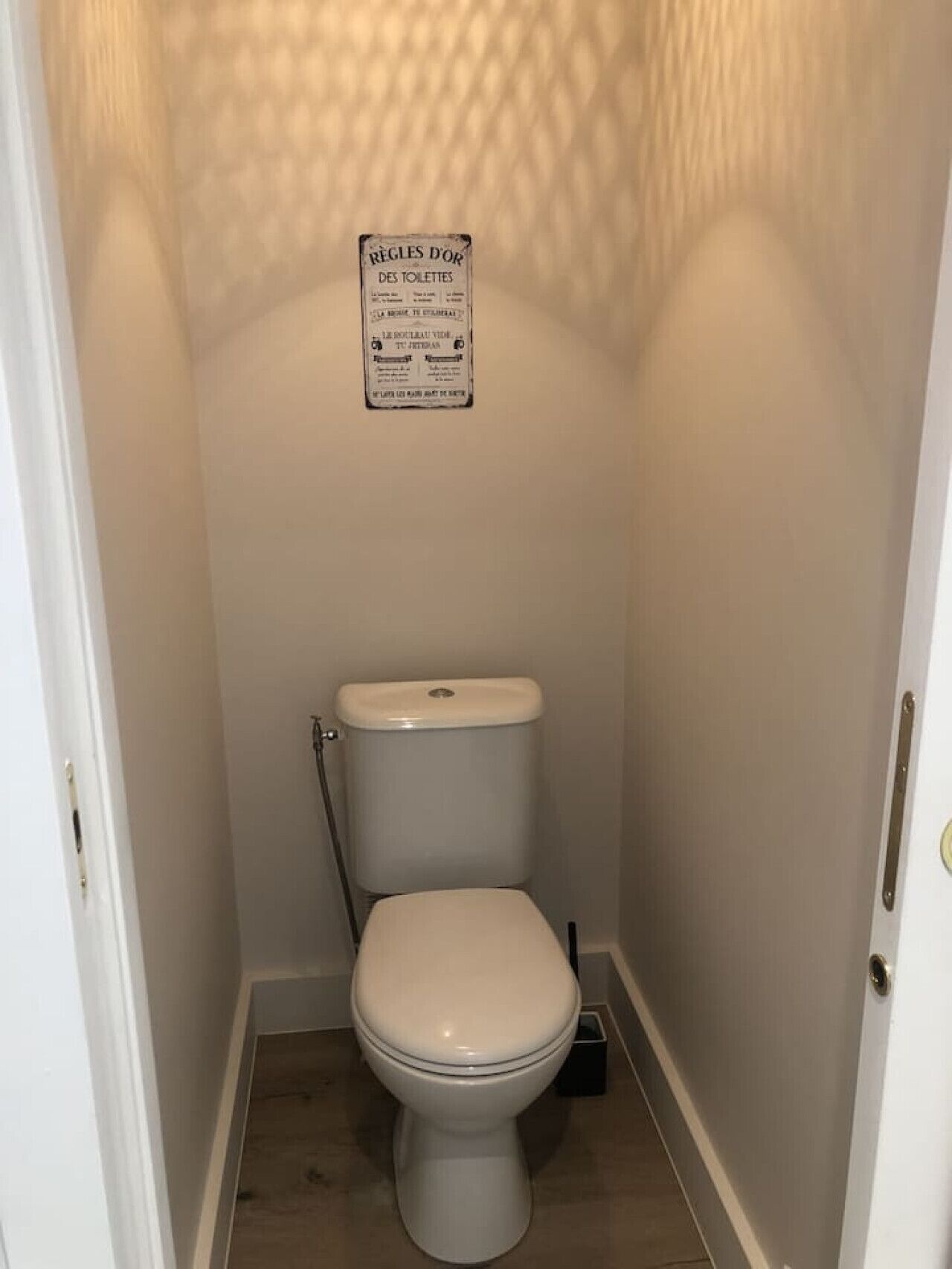 Un baño pequeño y estrecho con inodoro, pared blanca y un letrero sobre el inodoro.