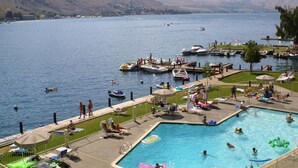 A swimming pool area with a view of a lake and boats, surrounded by a deck with lounge chairs and umbrellas. - Welcome to Wapato Point, Manson, WA (Manson)