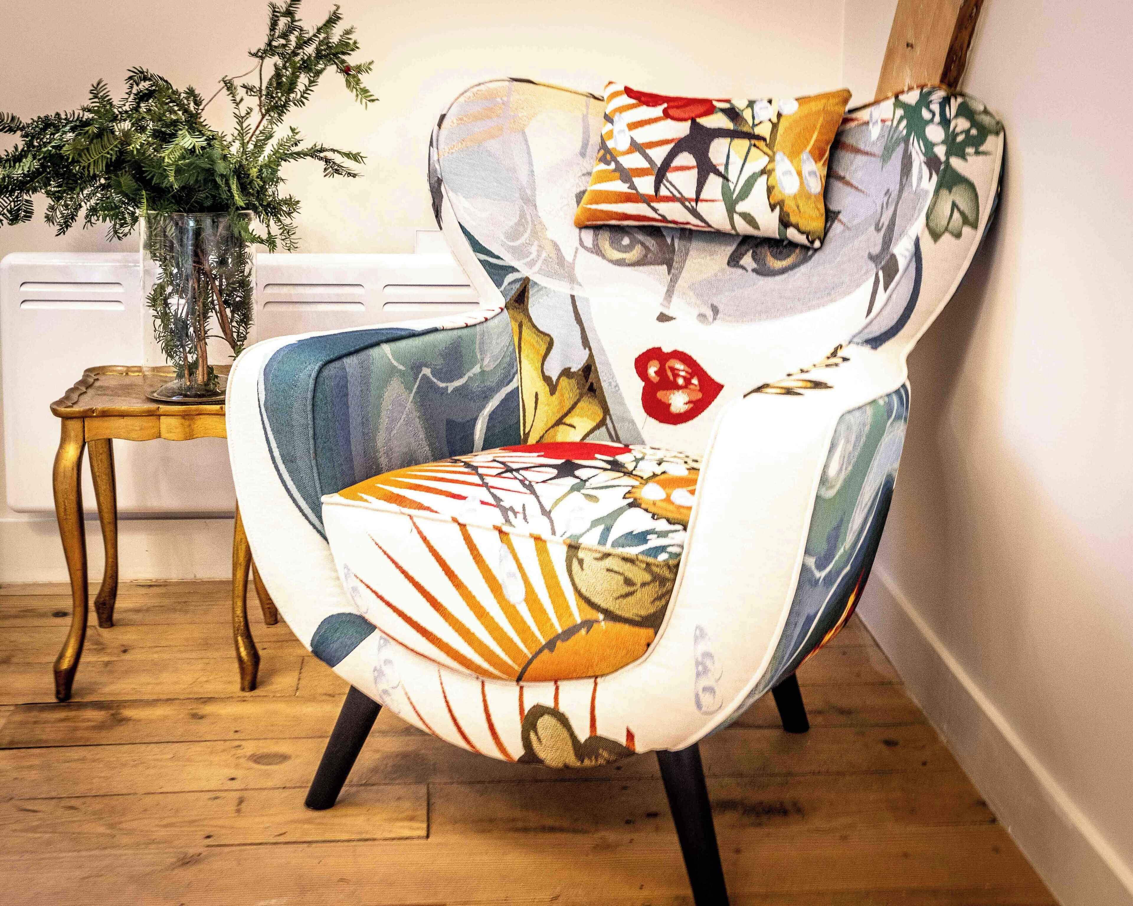 Een bijzonder vormgegeven fauteuil met een levendig, abstract patroon, geplaatst in een kamer met houten vloer en een klein bijzettafeltje.