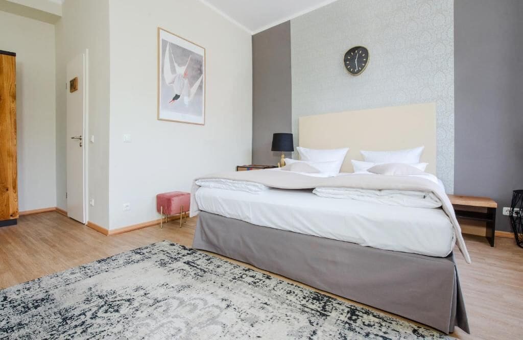 A bedroom with a bed, bedside table, lamp, and a clock on the wall.