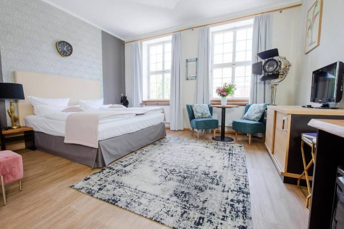 Ein Hotelzimmer mit Bett, Schreibtisch, Sessel, Fernseher und Lampe.