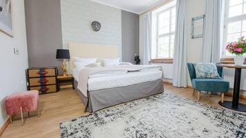 Una habitación de hotel con cama, mesita de noche, lámpara, tocador, silla y vistas al exterior por la ventana.