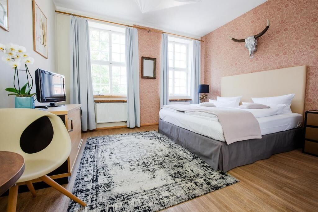A hotel room with a bed, a desk, a television, and a large window.