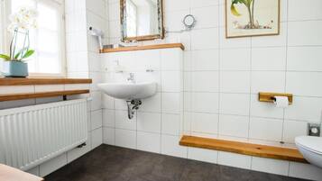 A bathroom with a white sink, wooden shelves, a radiator, and a toilet.