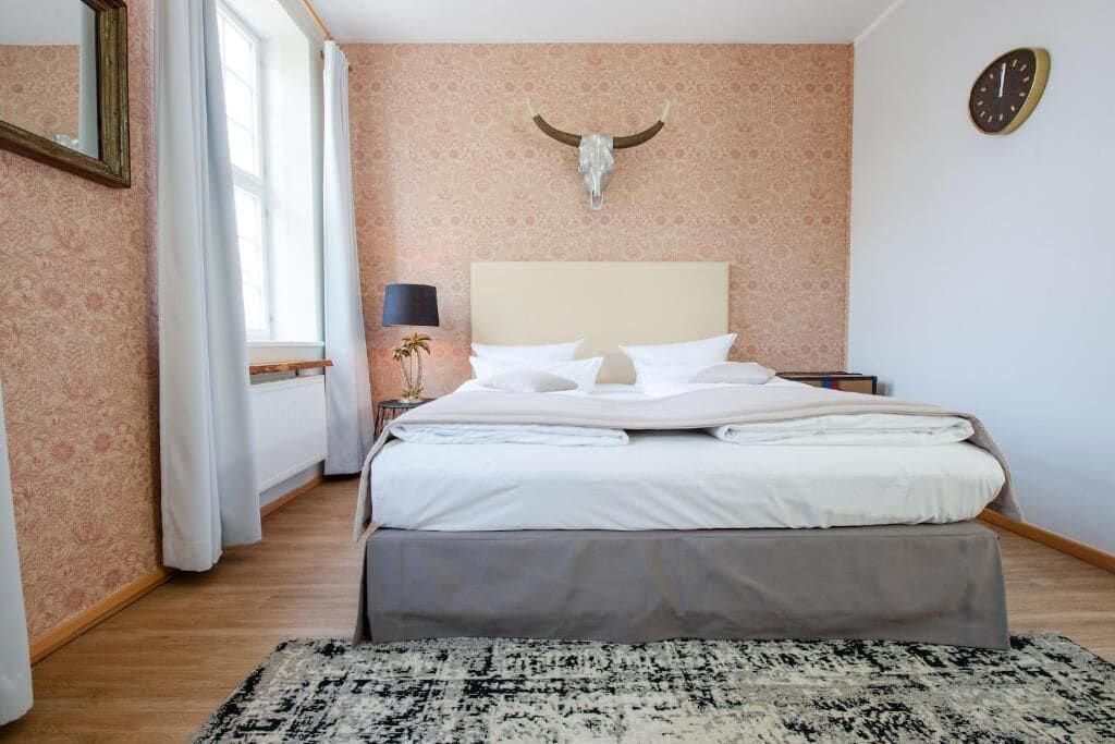 Een slaapkamer met een groot bed, een hoofdbord, een hangklok en een decoratie van een stierenhoofd.