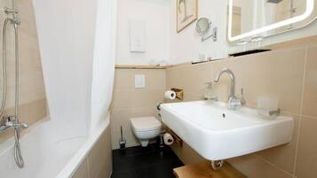 Un baño con bañera, inodoro, lavamanos y espejo con iluminación.