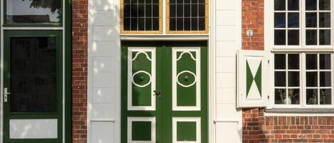 Un edificio tradicional con puerta verde y detalles blancos, paredes de ladrillo y una ventana con marco blanco.