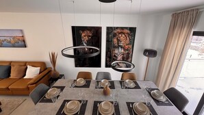A modern dining area with a rectangular table set for six, surrounded by six chairs. There are two large framed artworks on the wall above the table. - New vacation home on the outskirts (Eupen)