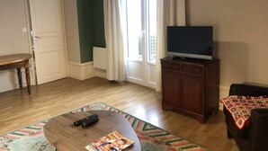 Un soggiorno con pavimento in legno, una televisione su un mobile, un tavolino da caffè con un telecomando e una porta che dà su un'altra stanza.