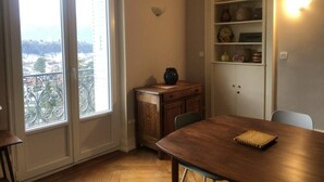 Zona pranzo con tavolo in legno, sedie, un mobile contenitore con oggetti decorativi e vista attraverso un'ampia finestra.
