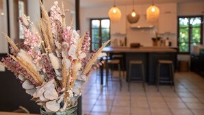 Cozinha moderna com ilha central, iluminação pendente e um vaso de flores secas em primeiro plano.