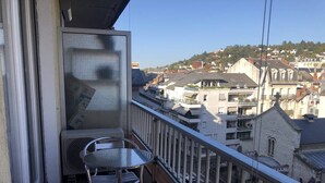 Un balcón con mesa y sillas de metal, con vistas a una zona residencial con casas y una colina al fondo.