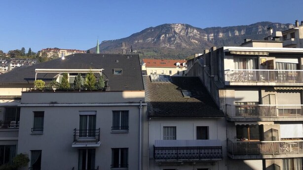 Un edificio residencial con techo plano, varios balcones y vistas a una cordillera.