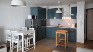 A modern kitchen with dark blue cabinets, a white dining table with chairs, and a small wooden stool. - Appartement 66m² 2 chambres, garage et terrasse (Aix-les-Bains)