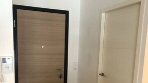 A hallway with two doors, one wooden and one white, and a light switch on the wall. - Appartement 66m² 2 chambres, garage et terrasse (Aix-les-Bains)