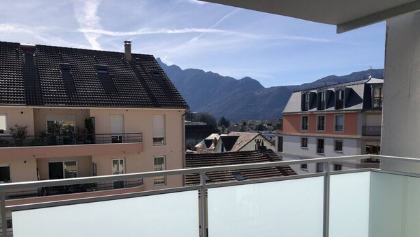 Un balcón con vistas a edificios vecinos y montañas.