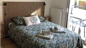 Un dormitori amb un capçal de fusta, un llençol estampat amb flors i vistes a l'exterior a través d'una porta de vidre.