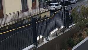 Un carrer residencial amb cases, una tanca de metall negre i cotxes aparcats.