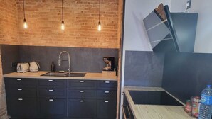 A modern kitchen with a brick wall, a large black cabinet, a sink, and a wooden countertop. - Le Loft Des Arts (Thonon-les-Bains)
