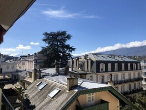 Blick auf eine Stadtlandschaft mit Gebäuden, darunter ein markanter Baum und ein Gebäude mit geneigtem Dach.