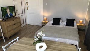 A hotel room with a wooden table, a TV on a dresser, a bed with two pillows, and bedside lamps. - Studio 25m², avec parking et balcon, centre-ville (Aix-les-Bains)