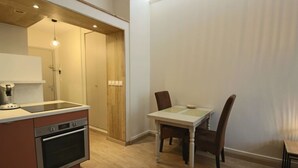 Una cocina compacta con horno integrado, una pequeña mesa de comedor con dos sillas y una puerta de madera que da a otra habitación.