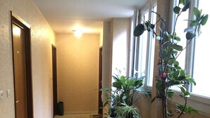 Un pasillo con suelo de madera, una pequeña mesa con plantas en macetas y una puerta a la izquierda.