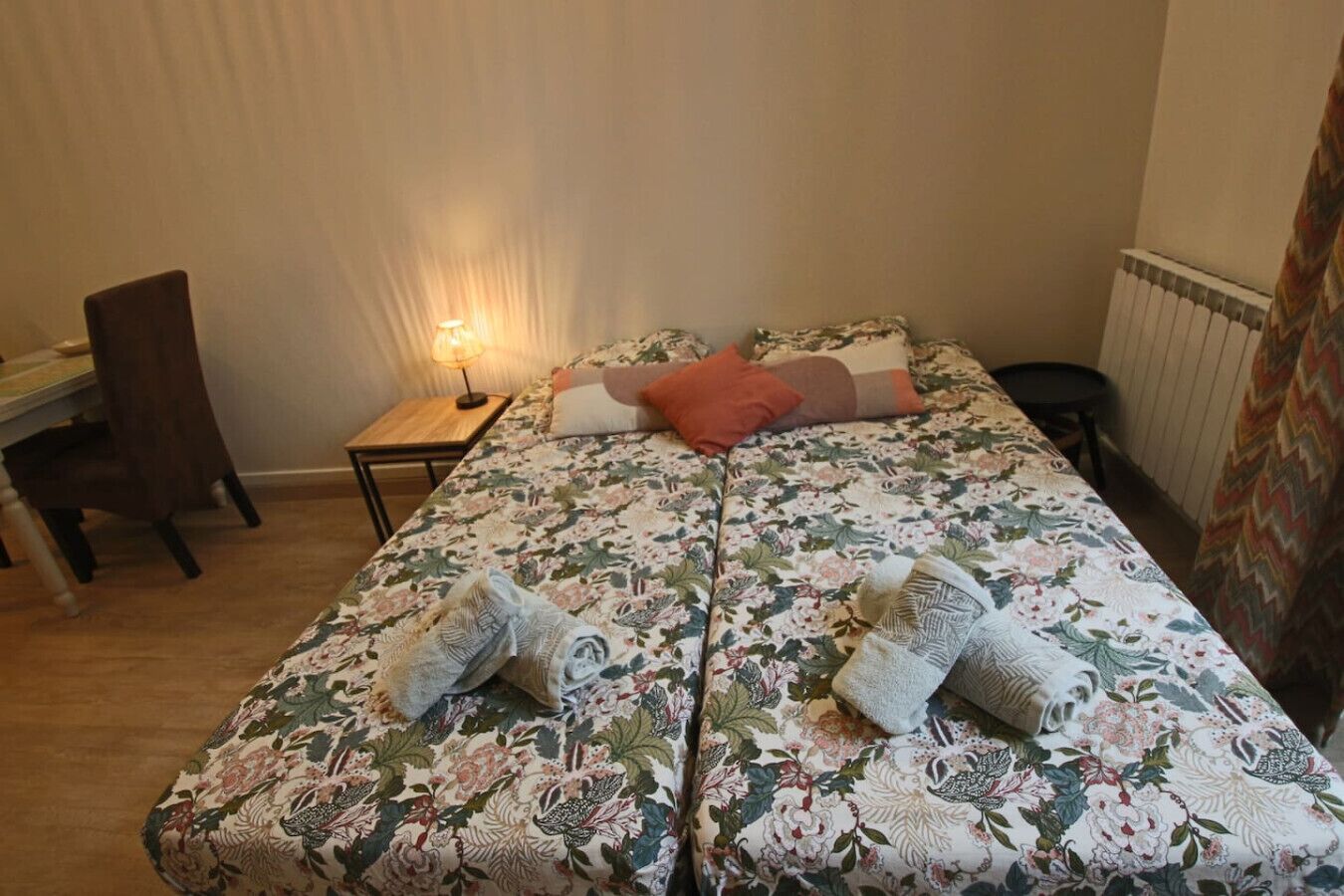 Et soveværelse med blomstret sengetæppe, et skrivebord med lampe og en stol.