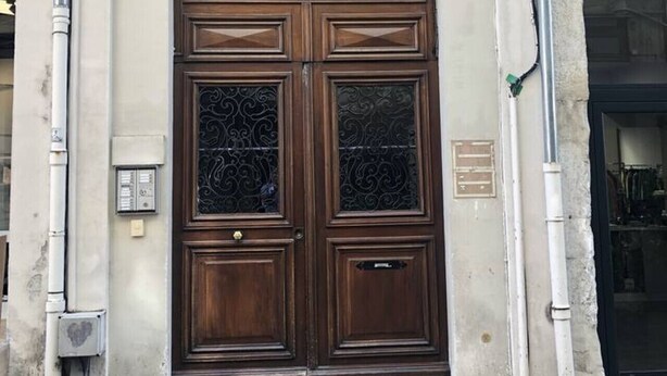Puerta doble de madera con paneles de vidrio, número 21, en la fachada de un edificio con ventanas de arco y suelo adoquinado.
