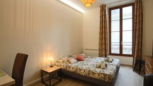Un dormitorio con cama, mesita de noche, silla, escritorio y ventana con cortinas.